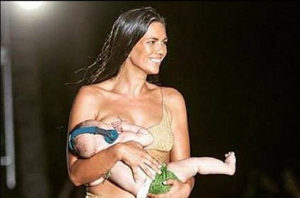 Model breastfeeds baby while walking ramp.